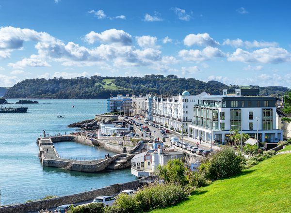 A photograph of part of the Plymouth coastline on a bright sunny day. A row of large white hotels beneath a blue sky.