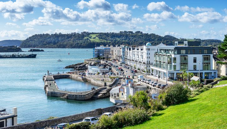 A photograph of part of the Plymouth coastline on a bright sunny day. A row of large white hotels beneath a blue sky.