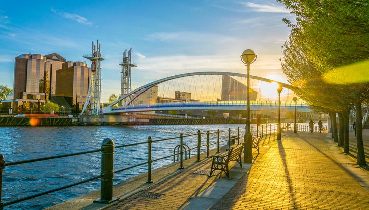 A rising sun shines through a view of a bridge over the water at Salford Quays
