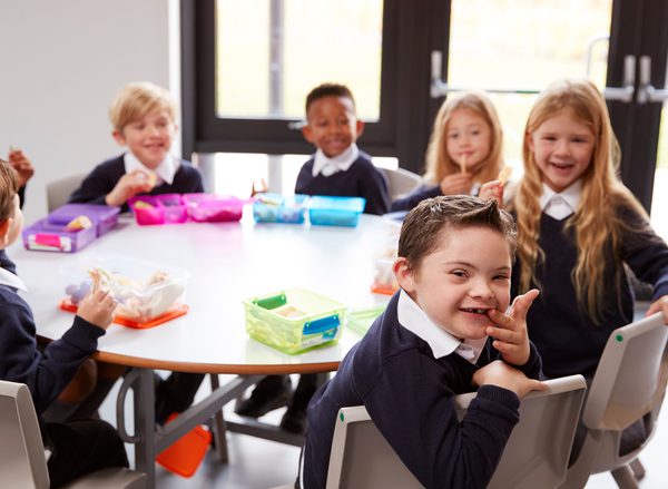 A group of children sit around a table at primary school. A little boy smiles into the camera