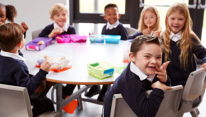 A group of children sit around a table at primary school. A little boy smiles into the camera