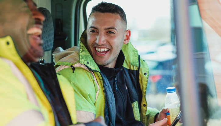 Two male construction workers in high vis jackets laughing together in a van