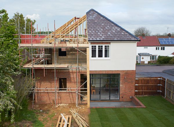 A house halfway through being built: half of it is complete and the other half reveals exposed timbers and scaffolding