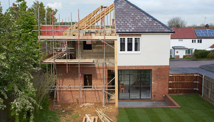 A house halfway through being built: half of it is complete and the other half reveals exposed timbers and scaffolding