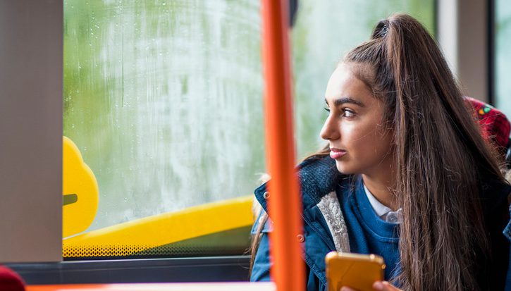 A young woman with a long ponytail sits looking out of a bus window