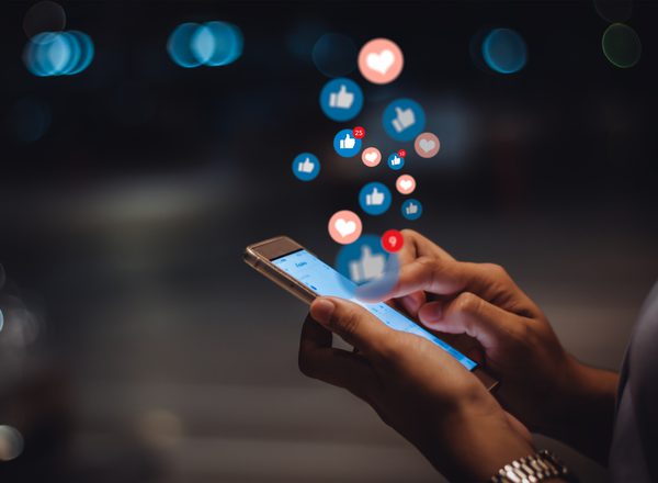 Someone's hands holding a mobile phone, with social media likes and heart icons floating out of it like bubbles