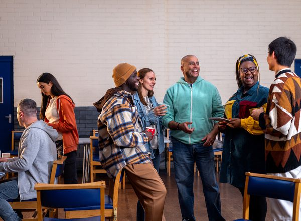 Adults standing in a circle and talking to each other about their mental wellbeing. There is a staff member sitting to the left of them in the frame sitting next to a table. The community centre is located in Seaton Deleval in the North East of England.
