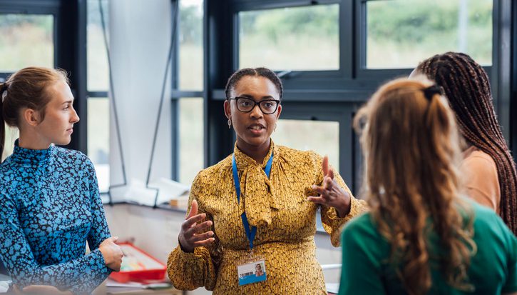 A secondary school teacher talking with her sixth form students in class.