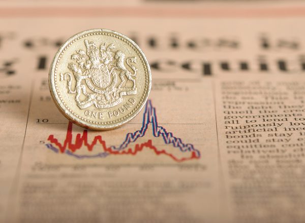 A pound coin sits on top of a newspaper showing an image of a line graph