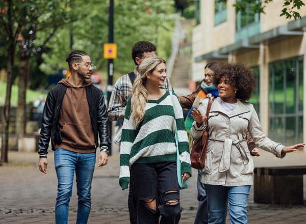 A front three quarter length view of a small group of university students walking together talking in the city on an autumn day in Newcastle, England