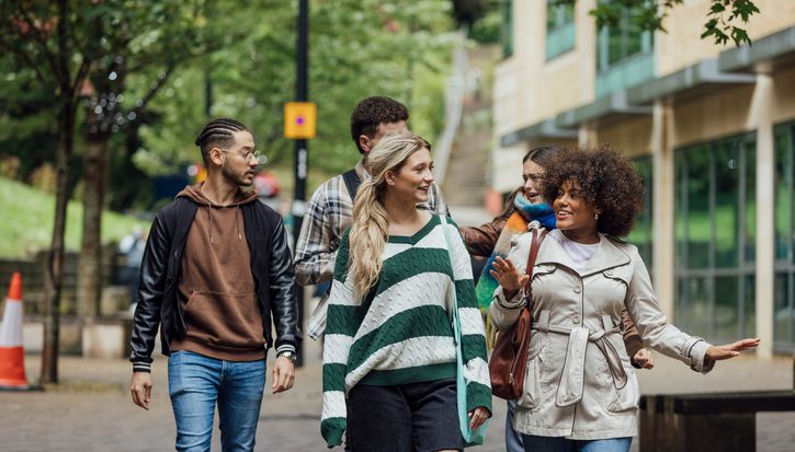 A front three quarter length view of a small group of university students walking together talking in the city on an autumn day in Newcastle, England