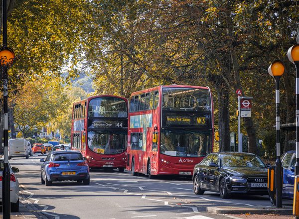 A two way street with busy traffic of driving cars and double-decker buses in autumn