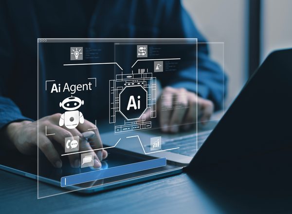 A person sits at a desk in front of a laptop. A semi-transparent screen shows a digital AI agent