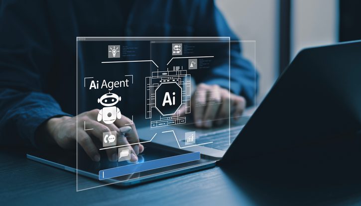 A person sits at a desk in front of a laptop. A semi-transparent screen shows a digital AI agent