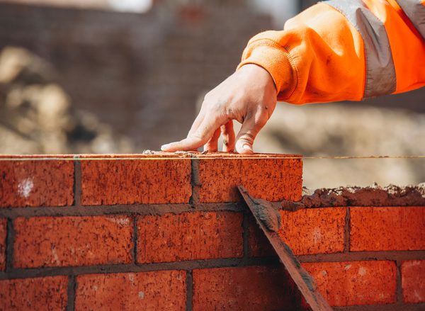 A close up photo of a bricklayer smoothing cement between a layer of red bricks