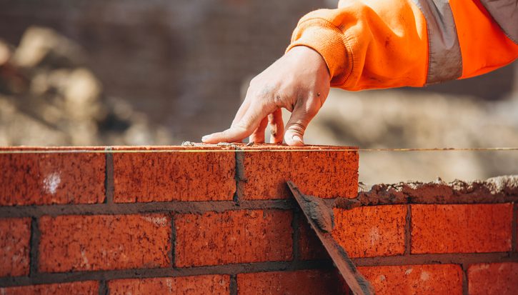 A close up photo of a bricklayer smoothing cement between a layer of red bricks