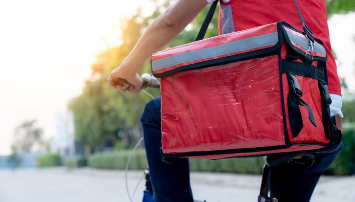 Young male delivery cyclist working part-time, riding through city streets with food backpack on.