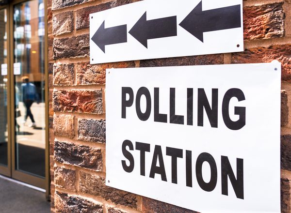 A close up photograph of a polling station sign on the outside of a building