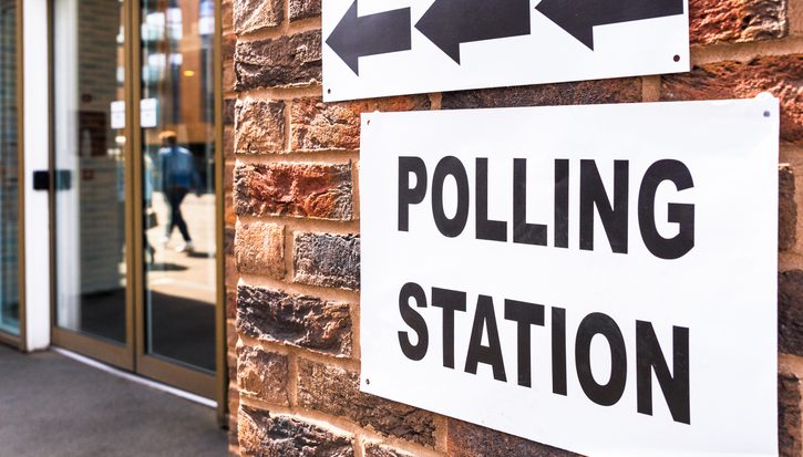 A close up photograph of a polling station sign on the outside of a building