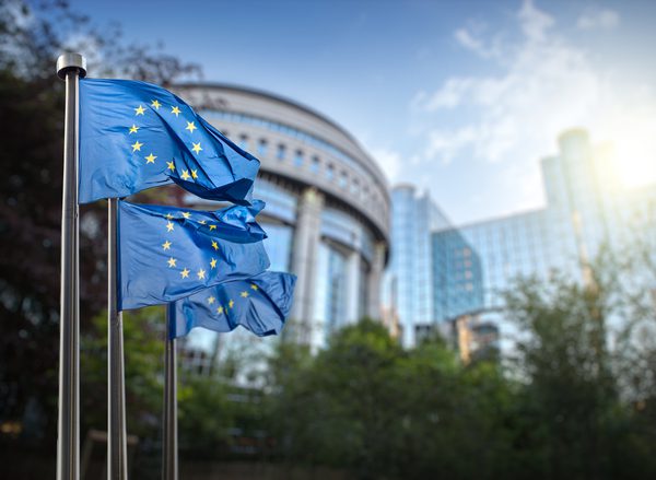 Three EU flags outside a large glass and steel building in Brussels, Belgium