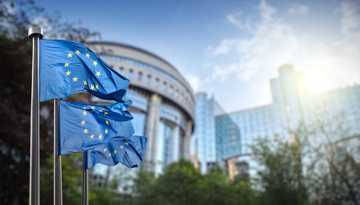 Three EU flags outside a large glass and steel building in Brussels, Belgium