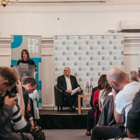 Audience facing Emma Norris, who is stood at a lectern, and Ed Davey, who is sat to the right.