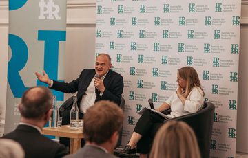Ed Davey and Sarah Mulley sat in front of IPPR banners. Ed Davey is speaking into a microphone.