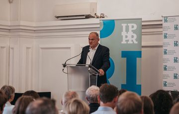 Audience facing Ed Davey, who is stood at a lectern speaking.