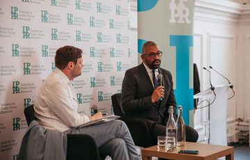 James Cleverly and Harry Quilter-Pinner sat in front of IPPR banners. James Cleverly is speaking into a microphone.