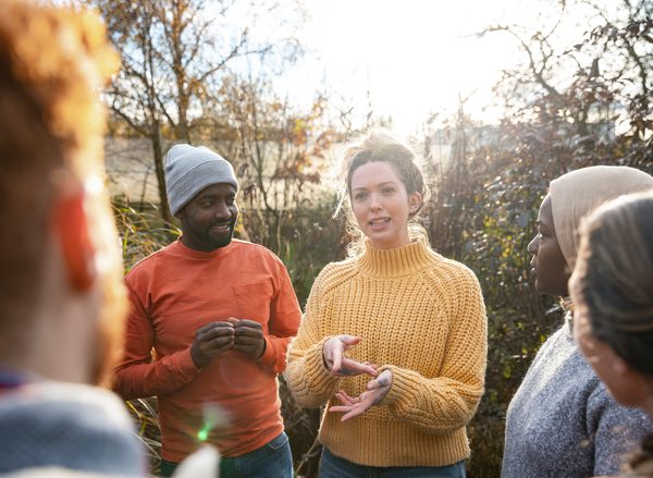 A woman in a yellow jumper is explaining something to a diverse group of volunteers